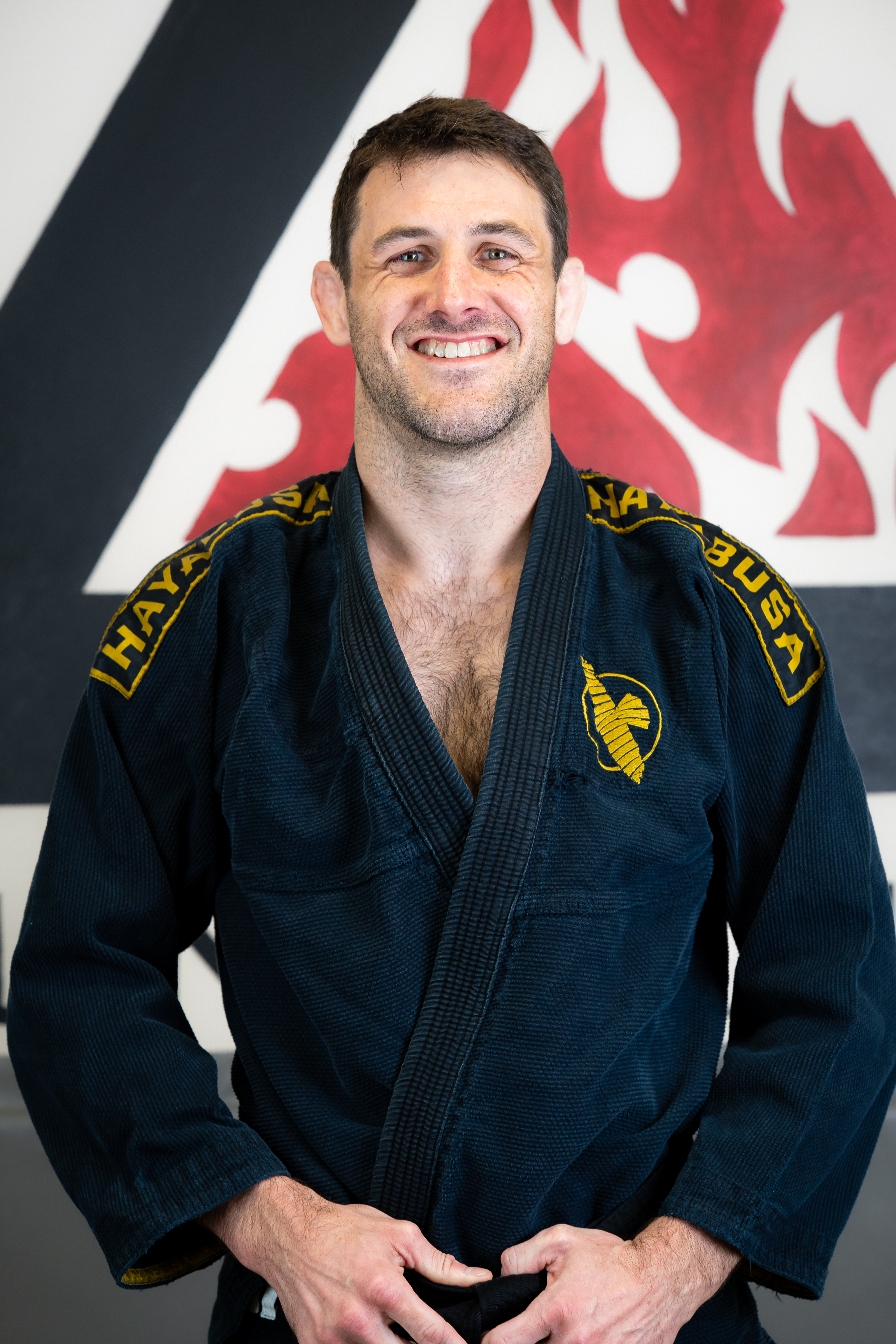 Handsome man in a jiujitsu gi smiling in front of the Bellingham BJJ Logo